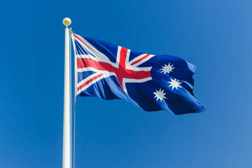 Close-up of Australian flag waving in the wind against clear blue sky. Symbol of national pride and unity