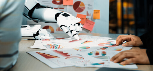 A human and robot work together in a modern office, analyzing various charts and graphs,...
