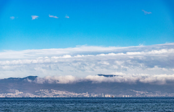 Expansive Coastal City View Across a Wide Bay or Harbor with Dense Urban Skyline Buildings Under a Dramatic Sky Filled with Heavy Dark Clouds. Impressive Landscape or Seascape Scene from Gulf.