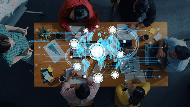 A diverse group of professionals engages in a collaborative business meeting with digital overlays of a world map, symbolizing innovation and strategy development in an office setting. Trope - Powered by Adobe