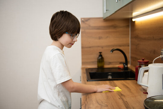 Young boy wiping a wooden kitchen countertop with a sponge.