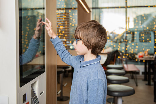 A boy using a touchscreen kiosk to place an order in a modern cafe interior with warm bokeh lights.