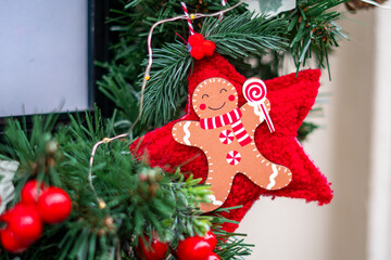 Christmas decoration featuring gingerbread figure on red star hanging among green branches with berries and small lights