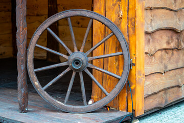Obraz premium Old wooden wagon wheel leaning against the wall of a wooden booth standing on a dark wooden platform