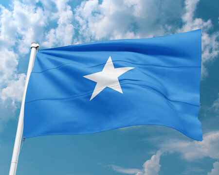 Realistic close-up of the Somalia flag waving on a tall flagpole under a bright sky with soft scattered clouds, showing smooth wind motion, vivid blue colors, and a clear atmosphere of national pride.