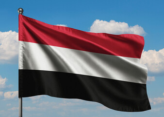 Realistic close-up of the Yemen flag waving on a tall flagpole under a bright sky with soft scattered clouds, showing smooth wind motion, sharp fabric details, vivid colors, and a clear sense 