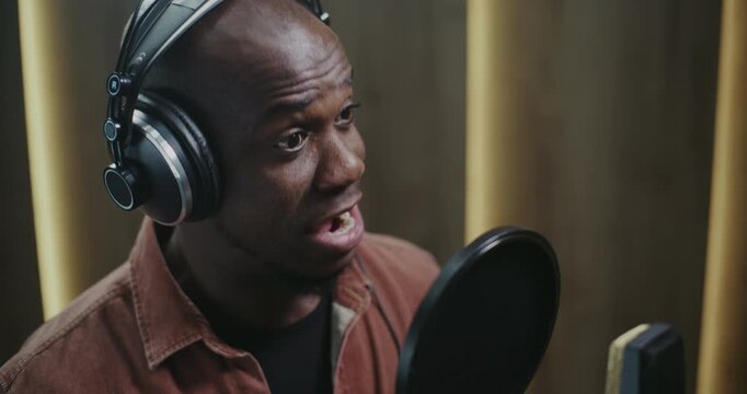 Male Voice Actor Delivering Dynamic Film Dubbing. Wearing Headphones and Facing Studio Microphone With Pop Filter, Man Records Expressive Lines With Strong Character Emotion and Vocal Precision.