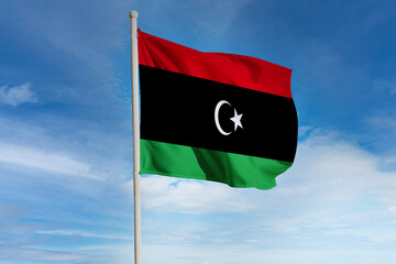 Realistic close-up of the Libya flag waving on a tall flagpole under a bright sky with soft scattered clouds, showing smooth wind motion, vivid colors, and a strong atmosphere of national pride.
