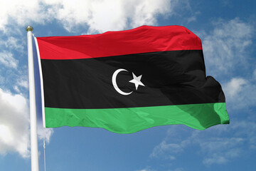 Realistic close-up of the Libya flag waving on a tall flagpole under a bright sky with soft scattered clouds, showing smooth wind motion, vivid colors, and a strong atmosphere of national pride.
