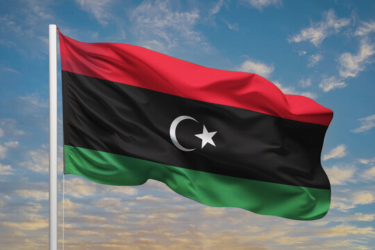 Realistic close-up of the Libya flag waving on a tall flagpole under a bright sky with soft scattered clouds, showing smooth wind motion, vivid colors, and a strong atmosphere of national pride.
