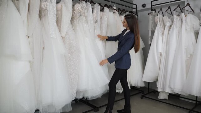 A young and lovely lady is selecting a wedding gown in a bridal boutique, examining the numerous gowns that are displayed on racks. A bridal boutique with a wide selection of dresses.