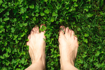 Bare feet standing on a green clover, a barefoot, spreading his fingers on the lush grass, a sun-drenched close-up shot that conveys texture, summer mood. Concept of a healthy lifestyle barefoot.