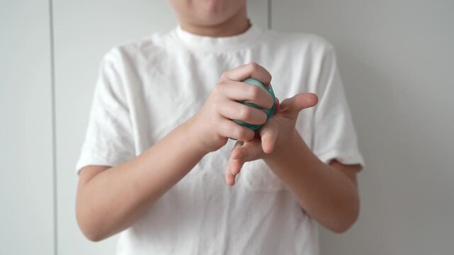 A 12-year-old child squeezing a blue stress ball, also known as hand putty or chewing gum for hands, against a light background.
