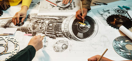 Hands collaborate over a large table filled with sketches and tools, focusing on the intricate...