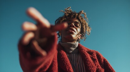 Low angle view of a stylish woman in a red coat reaching out against a clear blue sky, expressing confidence.
