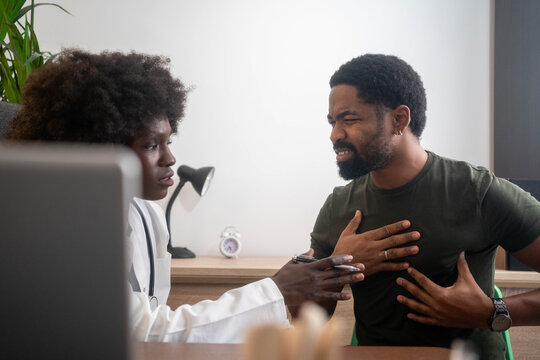Black man complaining of chest pain while female doctor examines him in clinic