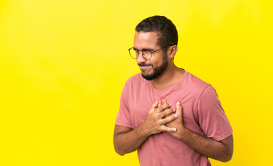 Young latin man isolated on yellow background having a pain in the heart