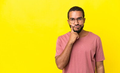 Young latin man isolated on yellow background and thinking