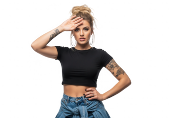 Young tattooed woman with blonde hair bun in black crop top and denim, hand on forehead, looking ahead with serious expression