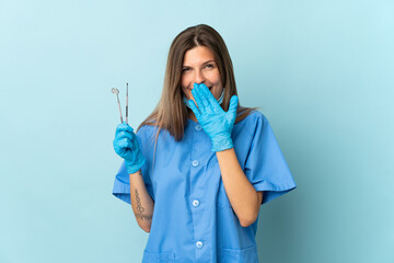 Slovak dentist holding tools isolated on blue background happy and smiling covering mouth with hand