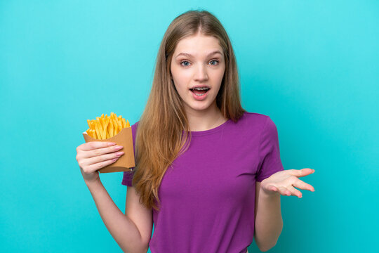 Teenager Russian girl catching french fries isolated on blue background with shocked facial expression