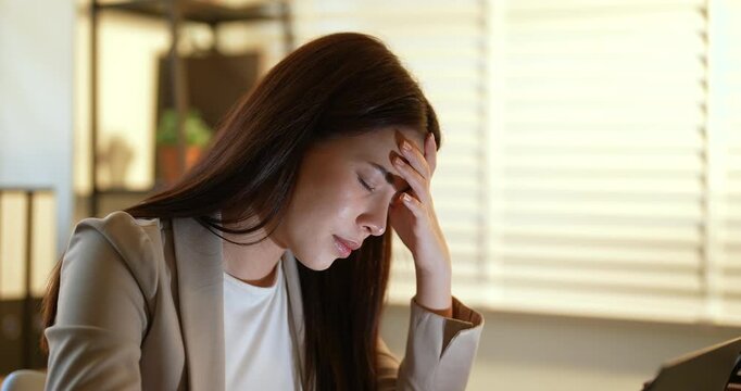 Asian female office worker leaning forward with closed eyes, exhausted after long working hours, struggling to stay awake while facing job stress, concept of fatigue and burnout in modern workplace