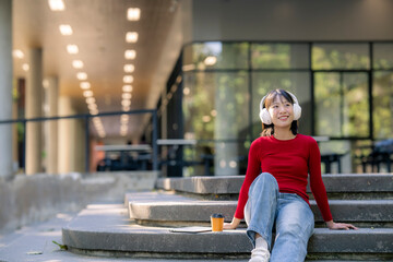 Woman student listening music with headphones on campus stairs