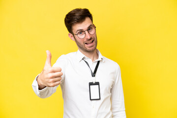 Young caucasian with ID card isolated on yellow background with thumbs up because something good...