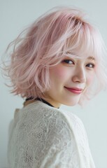 Portrait of a woman with stylish pink hair, smiling warmly, wearing a white lace top, and white background.
