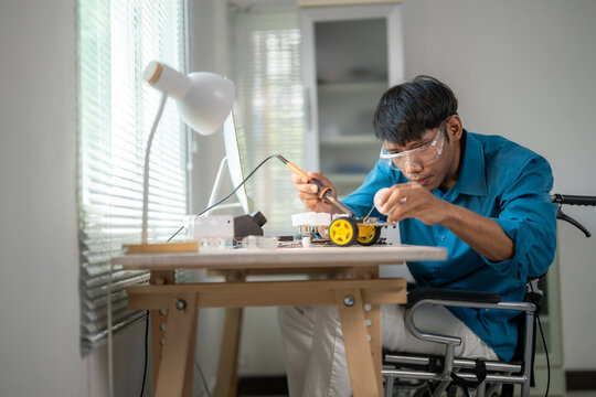 Asian engineer in wheelchair assembling a robot prototype using soldering iron
