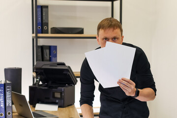 Suspicious man peeking over blank papers in office