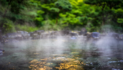The surface of a steamy hot spring (Onsen), with blurred natural greenery in the background.