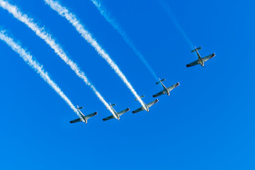 Airshow performance with aircraft, flight of pilotage team with colorful smoke trails. Planes and jets in the air. Flight show of air force team with group of planes in blue sky.