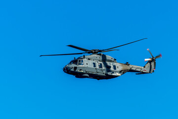 Military helicopter in the air on blue sky background. Gray patrol helix close up. Naval helicopter vehicle flying.