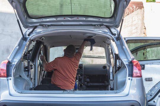 A man washes the headliner of a car. The car is parked.