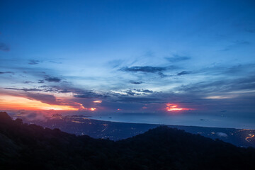 Breathtaking early morning panorama from Khao Luang Prachuap capturing mountains, ocean, glowing city lights and the first rays of dawn light in Prachuap Khiri Khan Province, Thailand.
