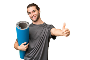 Young sport man going to yoga classes while holding a mat over isolated background giving a thumbs up gesture
