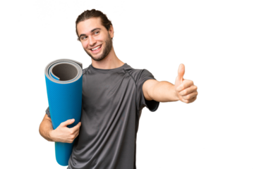 Young sport man going to yoga classes while holding a mat over isolated background giving a thumbs up gesture