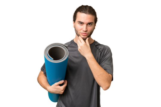 Young sport man going to yoga classes while holding a mat over isolated background thinking