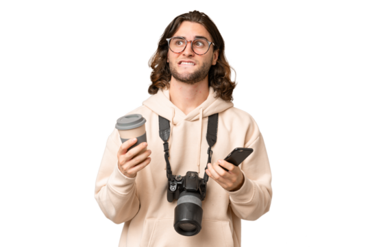 Young photographer man over isolated background holding coffee to take away and a mobile while thinking something