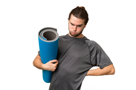 Young sport man going to yoga classes while holding a mat over isolated background suffering from backache for having made an effort