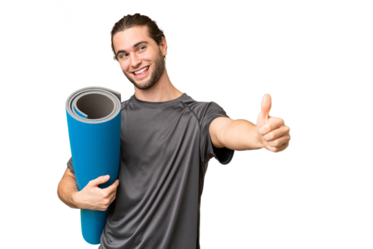 Young sport man going to yoga classes while holding a mat over isolated background giving a thumbs up gesture