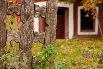 Faded wooden fence with intricate design framing a rustic building in autumn colors at sunset