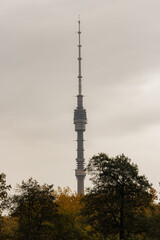 Tall communication tower rises above the autumn trees in a cloudy sky