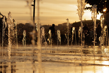 Evening golden hour shines over dancing water jets in a lively city square