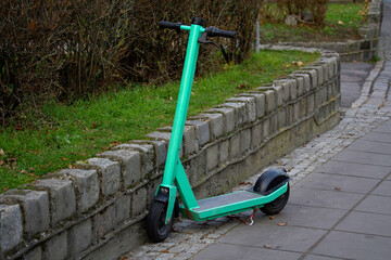 A green electric scooter parked on the sidewalk