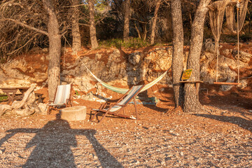 Cozy boho retreat in warm summer light, with hammock, deck chairs, and rustic details surrounded by nature. Summer holiday relaxation and peaceful outdoor getaway. Vacation concept.