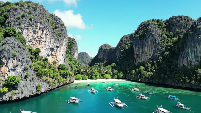 Aerial view of a stunning tropical bay with towering limestone cliffs, clear turquoise water, and traditional boats