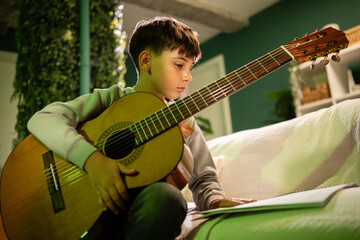 Young boy learning playing acoustic guitar at home