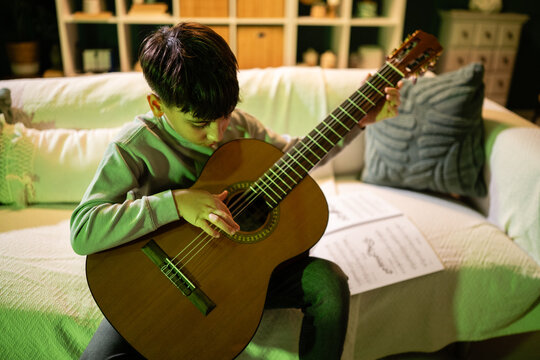 Young boy learning playing acoustic guitar reading sheet music - Powered by Adobe